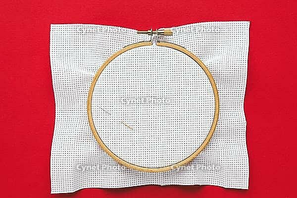 Embroidery hoop with white canvas and two needles placed on vibrant red background, minimalist flat lay symbolizing creativity, traditional craft and artistic inspiration, cross stitch [IBR123638390]
