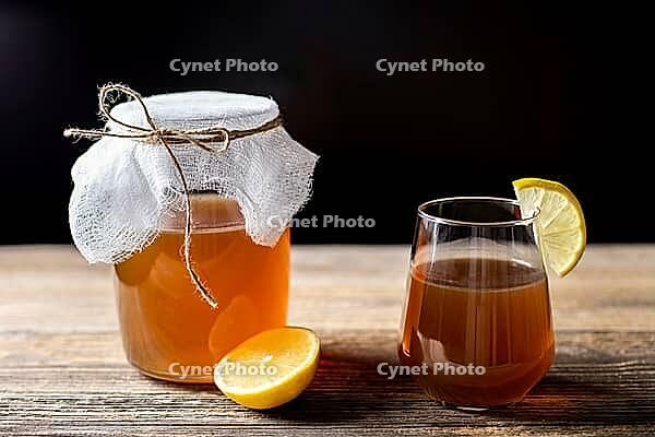 Raw fermented homemade alcoholic or non alcogolic kombucha superfood. Ice tea with healthy natural probiotic in glass with lemon slice on wooden background [IBR123639494]