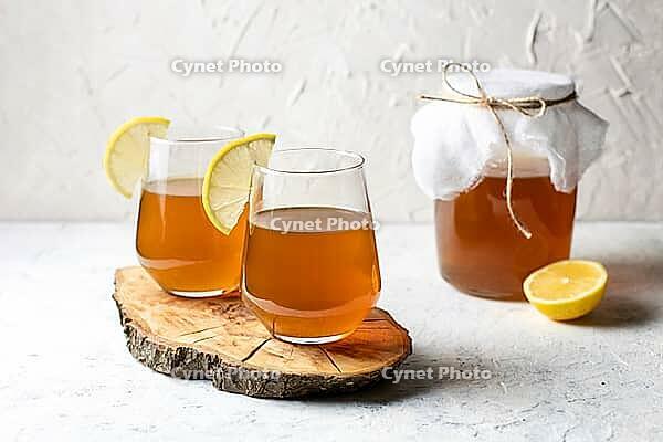 Raw fermented homemade alcoholic or non alcogolic kombucha superfood. Ice tea with healthy natural probiotic in glass with lemon slice on white background [IBR123639497]
