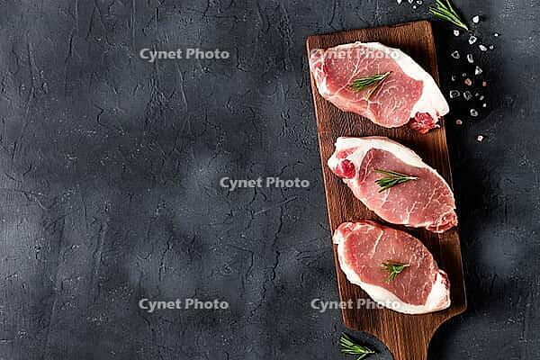 A pieces of raw fresh pork with rosemary on a cutting board on dark background. Meat with spices for recipes and cooking. Top view with copy space [IBR123639505]