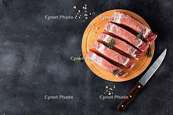 A pieces of raw fresh pork with rosemary on a cutting board on dark background. Meat with spices and knife for recipes and cooking. Top view with copy space [IBR123639506]