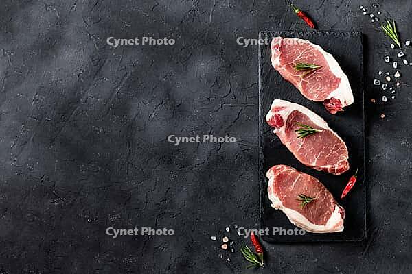 A pieces of raw fresh pork with rosemary on a cutting board on dark background. Meat with spices for recipes and cooking. Top view with copy space [IBR123639507]