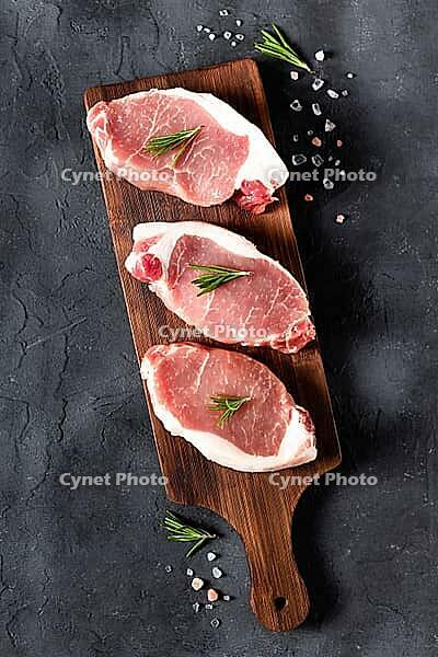 A pieces of raw fresh pork with rosemary on a cutting board on dark background. Meat with spices for recipes and cooking. Top view [IBR123639509]