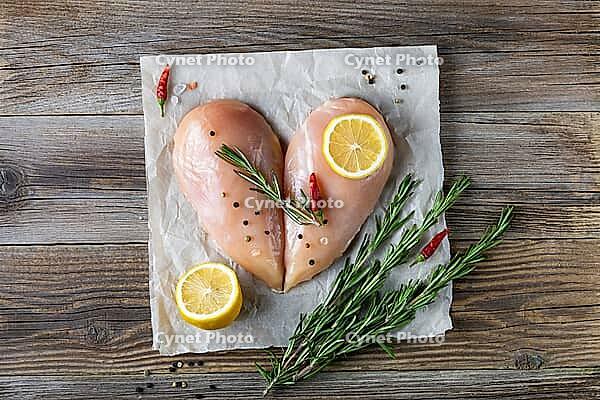 Raw chicken fillet in the shape of a heart with rosemary and spices on natural wooden background. Top view [IBR123639511]
