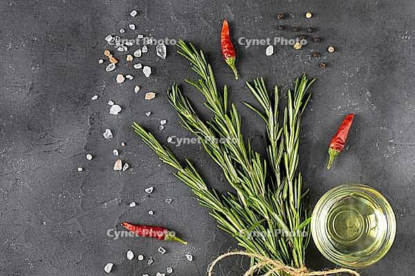 Bunch of green fresh rosemary with pepper, salt, lemon and oil on the dark stone background. Herbs and spices for recipes. Top view with copy space [IBR123639512]