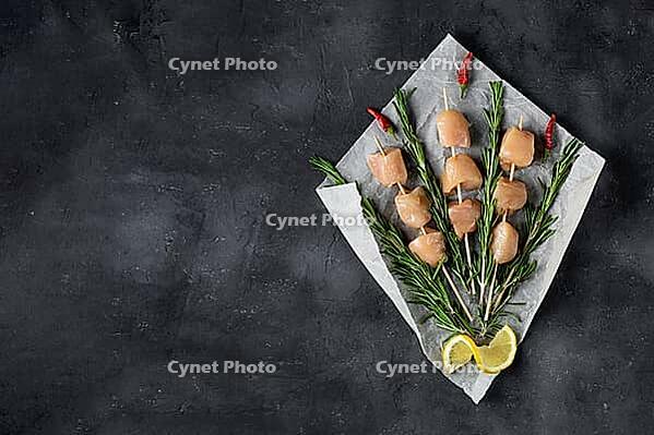 Raw chicken kebabs and rosemary in the form of a bouquet on a dark background. Food background, cooking ingredients. Top view with copy space [IBR123639515]