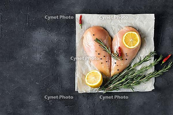 Raw chicken fillet in the shape of a heart with rosemary and spices on dark concrete background. Top view with copy space [IBR123639519]