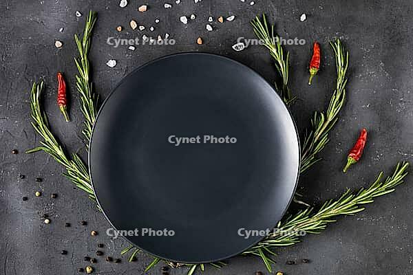 Empty black plate with rosemary branches and spices on a dark background. Top view with copy space [IBR123639523]