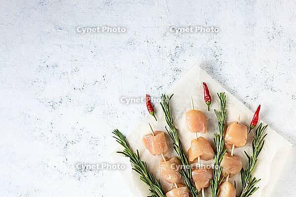 Raw chicken kebabs and rosemary in the form of a bouquet on a light background. Food background, cooking ingredients. Top view with copy space [IBR123639524]