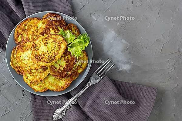 Fritters from zucchini in grey plate with sour cream sauce and greens. Vegetable pancakes of courgettes with green salad on grey background. Top view with copy space [IBR123639582]