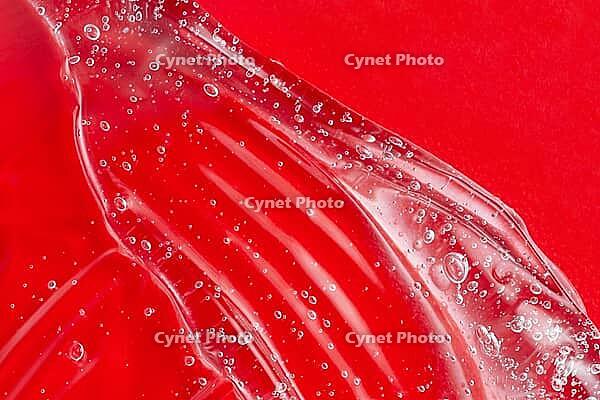 Transparent skincare product on red. Cosmetic gel smudge with bubble. Liquid lotion splash. Serum gel. Hyaluronic acid smear. Lubricant sample. Moisturiser with vitamin. Sexy jelly texture [IBR123646496]
