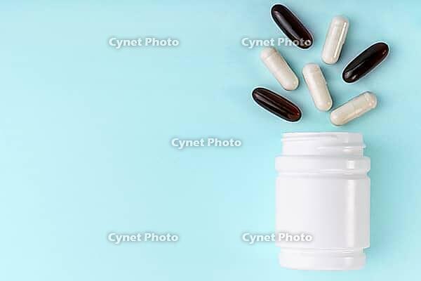White medical pills and capsules spilling out of bottle. Medication in white container on blue background. Healthcare, health insurance, medicine concept. Copy space, front view [IBR123646511]