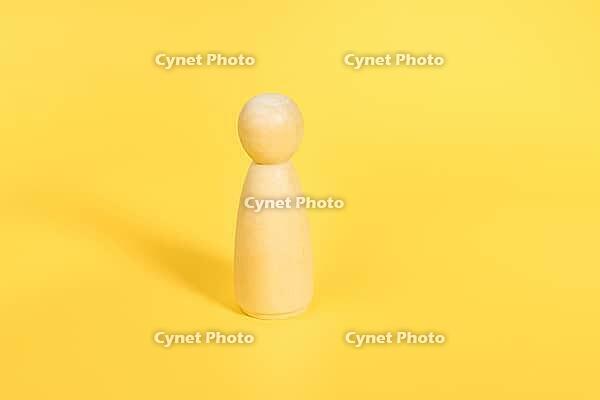 One wooden female figurine stands alone on yellow backdrop isolated. Confident independent person, mentor, coach, leader concept. Front view [IBR123646519]
