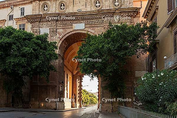 Close-up view of the archway of Porta Nuova in Palermo, Sicily, highlighting detailed stonework and decorative elements, framed by trees and illuminated by sunlight [IBR123646557]