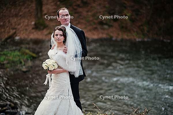 Lovely newlyweds background waterfall at cold autumn day [IBR123675131]