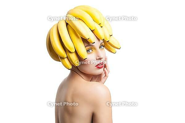 Beautiful fragile model with bunch of bananas on head looking away.Studio shot [IBR123723188]