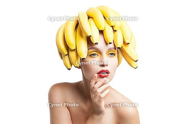 Beautiful fragile model with bunch of bananas on head looking away.Studio shot [IBR123723190]