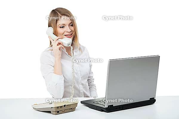 Young professional business woman working at her desk with laptop and smiling while calling and having telephone conversation over white background [IBR123723200]