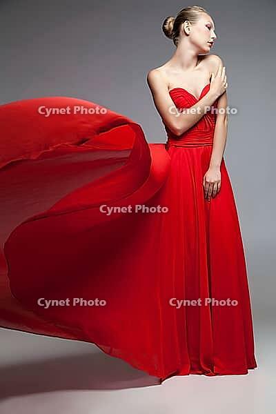 Portrait of young model posing in red dress with flying skirt.Studio shot [IBR123723221]