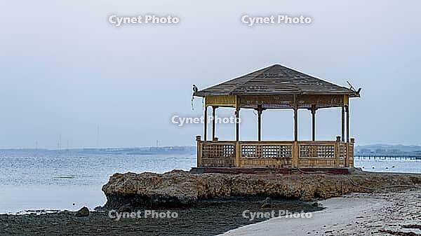 Lonely wooden pavilion on rocks on beach with cool, calm sea in the background, Shoni Bay, Egypt [IBR123769628]