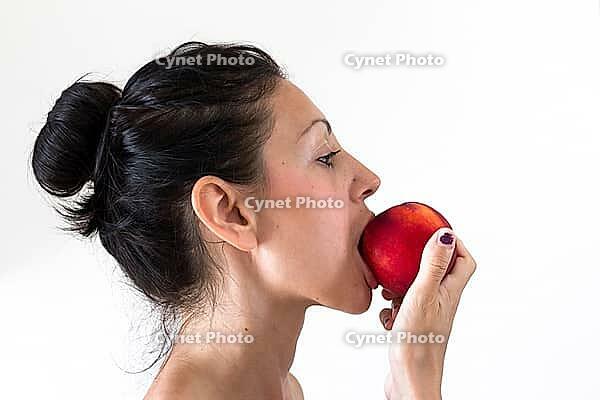 A girl while eating a peach, isolated on white background [IBR123878892]