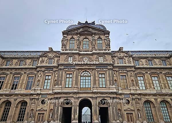 Paris, France - December 10, 2025: The ornate Renaissance facade and the iconic glass Pyramid of the Louvre Museum with multiple tourists scattered across the vast cobblestone courtyard [IBR123895590]