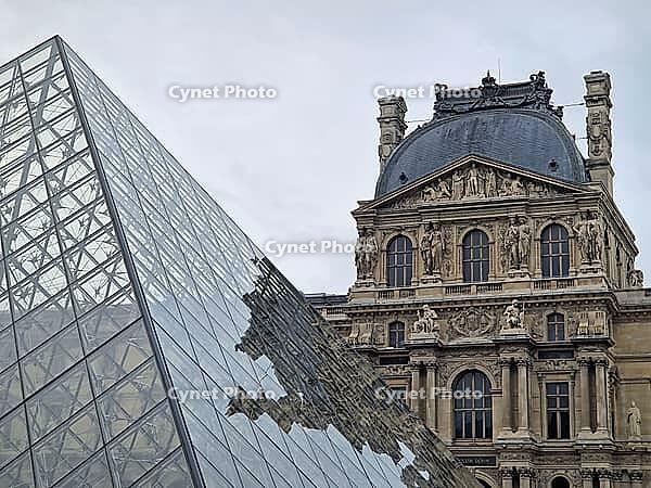 Paris, France - December 10, 2025: The ornate Renaissance facade and the iconic glass Pyramid of the Louvre Museum with multiple tourists scattered across the vast cobblestone courtyard [IBR123895591]