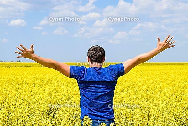 Free man in the field. The man raised his hands up. Field of flowering rape [IBR123999802]