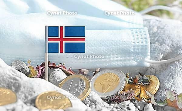 Icelandic flag with euro currency coins and a medical mask on rocky ground.International healthcare costs, cross-border medical funding, Europe and Iceland cooperation and global health finance [IBR124084099]