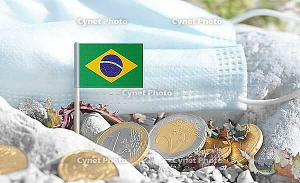Brazilian flag with euro currency coins and a medical mask on rocky ground.International healthcare costs, cross-border medical funding, Europe and Brazil cooperation and global health finance [IBR124084100]