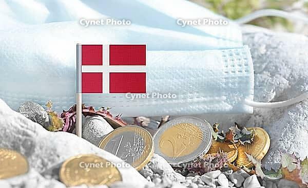 Danish flag with euro currency coins and a medical mask on rocky ground.International healthcare costs, cross-border medical funding, Europe–Denmark cooperation and global health finance [IBR124084115]