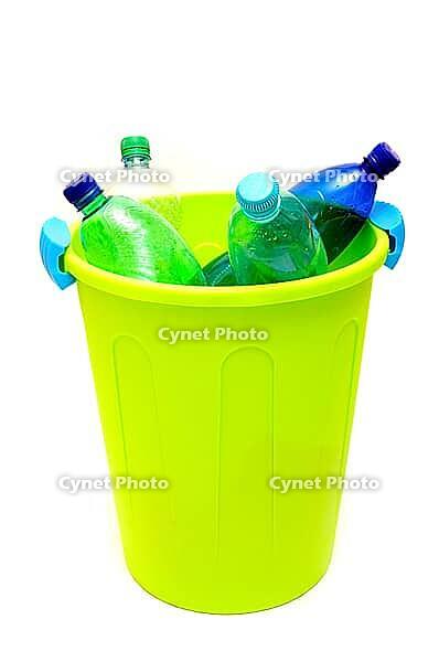 Green garbage bin filled with plastic bottles against white background [IBR124192771]