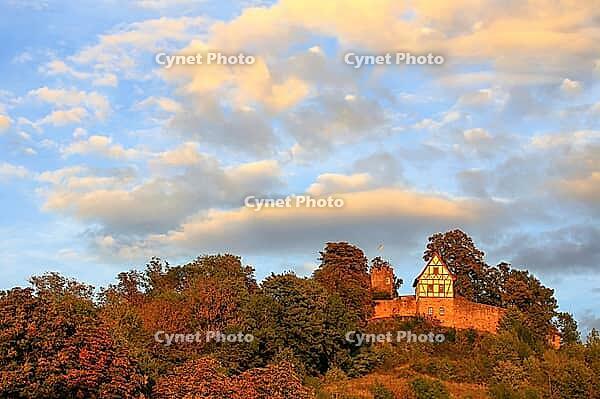 This atmospheric photo captures Königsberg Castle in Bavaria during the golden hour. The eye is drawn to the characteristic building with its red and white half-timbered gable, which was built on a massive stone wall. A square observation tower rises up b [IBR124192774]