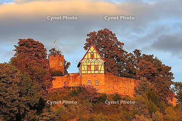 This atmospheric photo captures Königsberg Castle in Bavaria during the golden hour. The eye is drawn to the characteristic building with its red and white half-timbered gable, which was built on a massive stone wall. A square observation tower rises up b [IBR124192775]