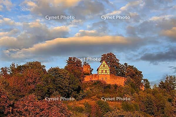 This atmospheric photo captures Königsberg Castle in Bavaria during the golden hour. The eye is drawn to the characteristic building with its red and white half-timbered gable, which was built on a massive stone wall. A square observation tower rises up b [IBR124192776]