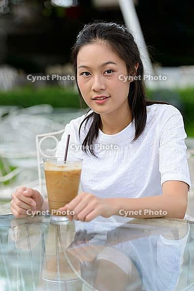 Portrait of young beautiful Asian woman relaxing at the coffee shop with nature outdoors [IBR124309059]