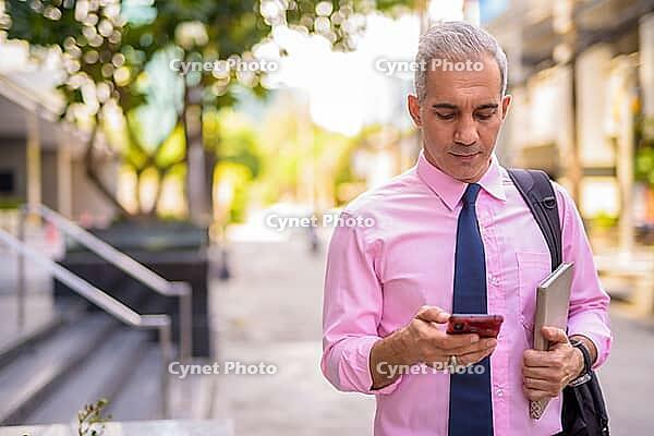 Portrait of handsome Persian businessman with gray hair in the city streets outdoors [IBR124309076]