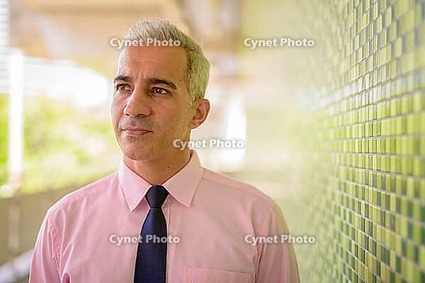 Portrait of handsome Persian businessman with gray hair at the footbridge in the city [IBR124309079]