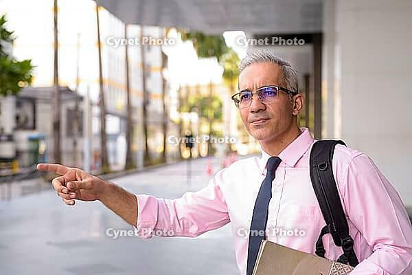Portrait of handsome Persian businessman with gray hair outside modern building in the city [IBR124309082]