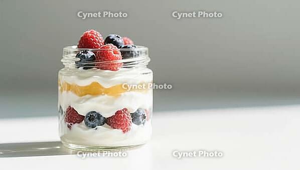 A glass of layered dessert with yoghurt, golden layer and fresh berries, minimalistically bright, delicious dessert, beautifully presented, AI generated [IBR124458897]