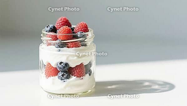 A glass with yogurt and fresh berries in the sun that casts a shadow on a white surface, delicious dessert, beautifully presented, generated by AI, AI generated [IBR124458906]