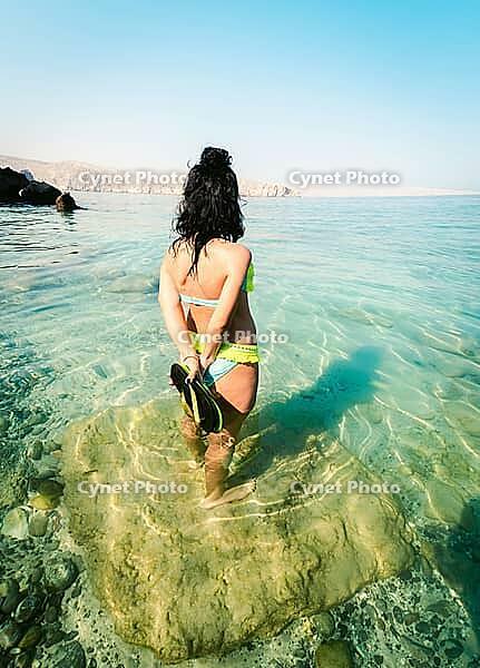 Back view pretty tourist woman stand in clear turquoise water in persian gulf Mirellas island. Oman coastline paradise. Musandam [IBR124458924]