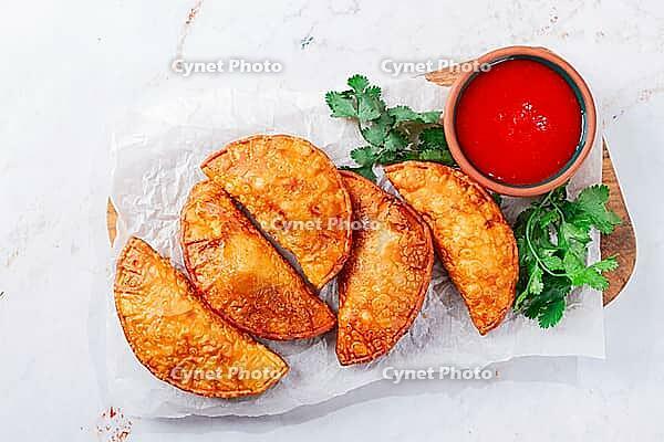 Fried mini chebureks, close-up, on a wooden chopping board, light background, no people [IBR124476264]