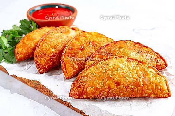 Fried mini chebureks, close-up, on a wooden chopping board, light background, no people [IBR124476266]