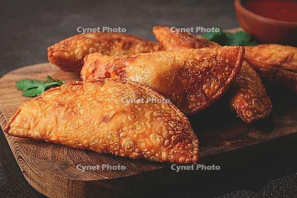 Fried mini chebureks, close-up, on a wooden chopping board, dark background, no people [IBR124476267]