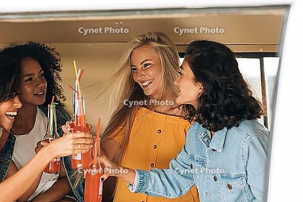 Four women toasting with bottles while sitting in camper van [IBR124491533]