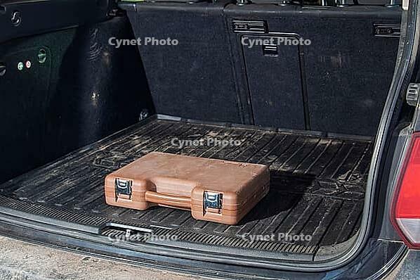 A single brown plastic case with silver clasps sits on a ribbed black rubber mat inside a car's cargo area, suggesting a journey or storage solution [IBR124491535]