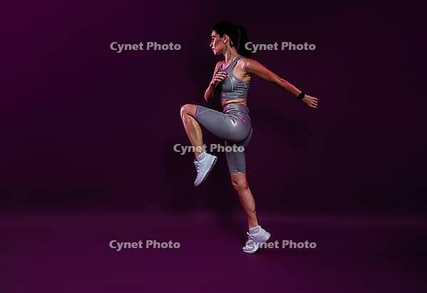 Full length of a young slim jogger practicing over a magenta backdrop. Female in silver fitness attire jumping [IBR124491536]