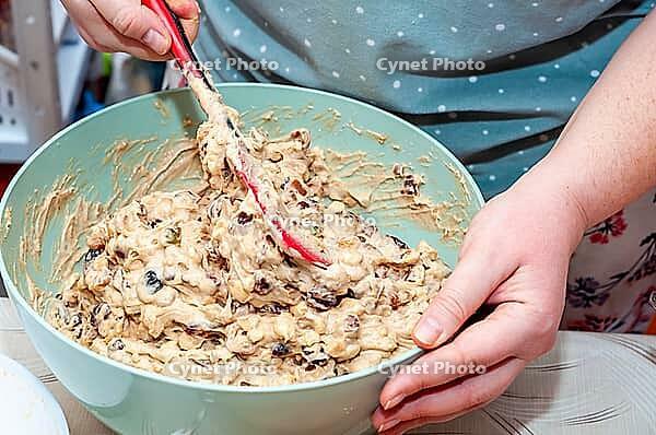 A person is mixing fruitcake batter in a large, turquoise bowl with a red spatula, ready to bake a delicious cake [IBR124491537]