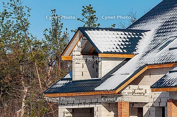 The construction of a home is in progress, with snow lightly dusting the roof and the block walls under a clear blue sky [IBR124491544]